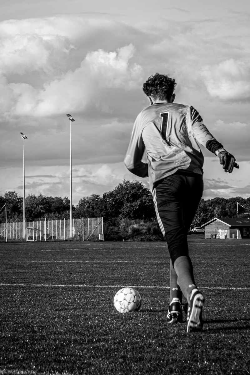 Photo by Elin Tabitha man in white long sleeve shirt playing soccer in grayscale photography